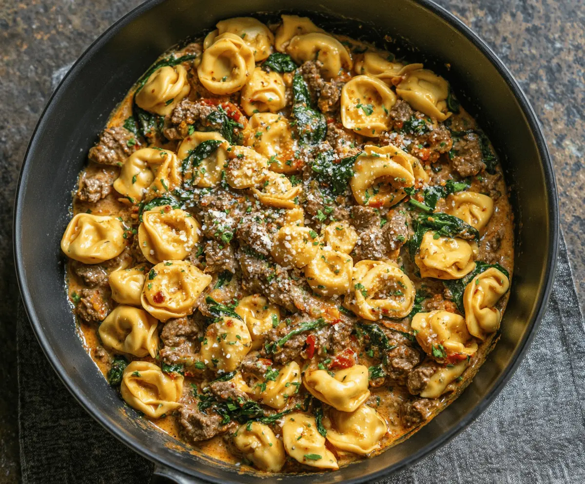 Creamy garlic butter beef and spinach tortellini dish garnished with fresh herbs, featuring tender tortellini filled with cheese and beef, topped with sautéed spinach and a rich garlic butter sauce.