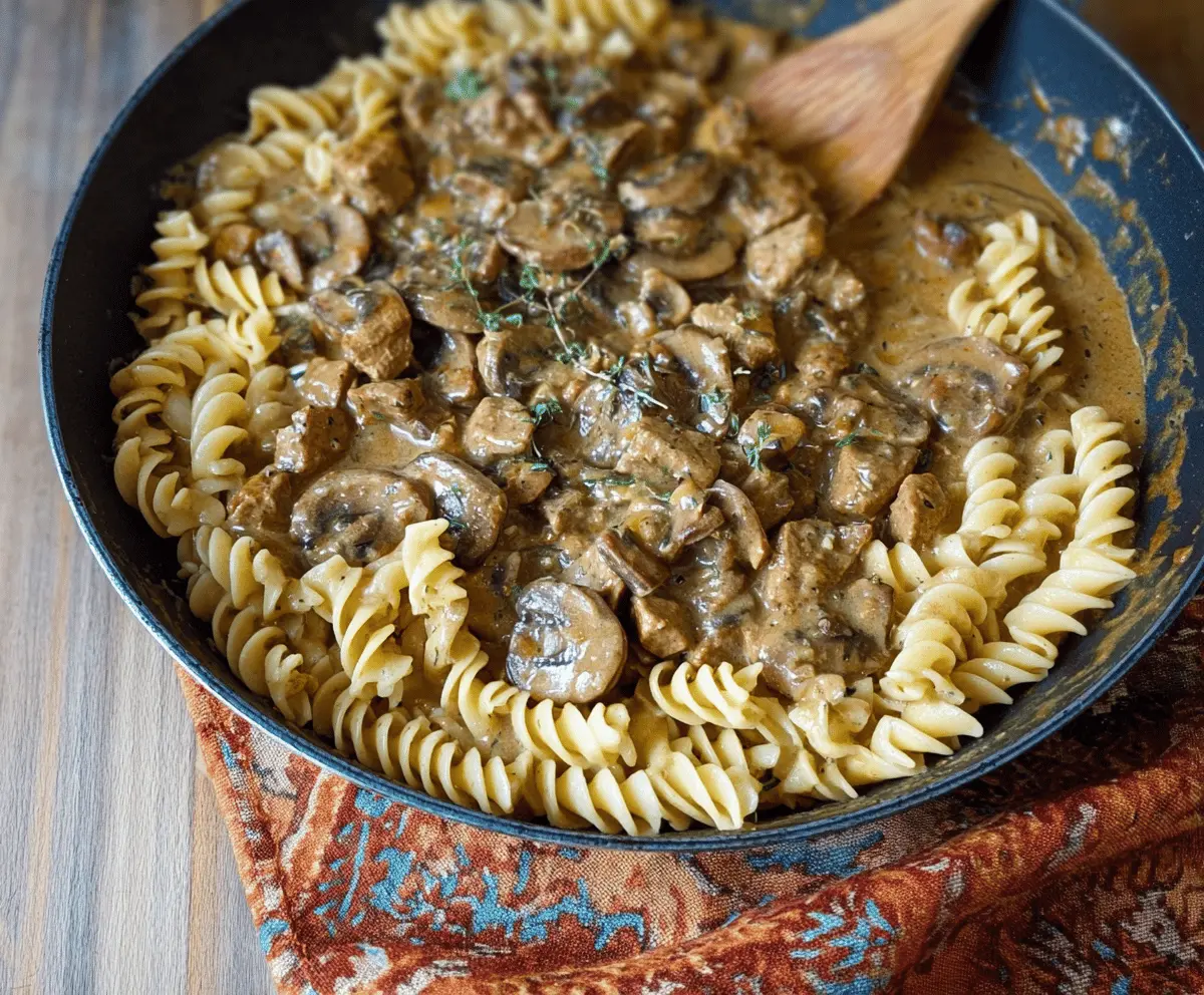 Creamy mushroom and seitan stroganoff served over noodles with fresh herbs in a bowl