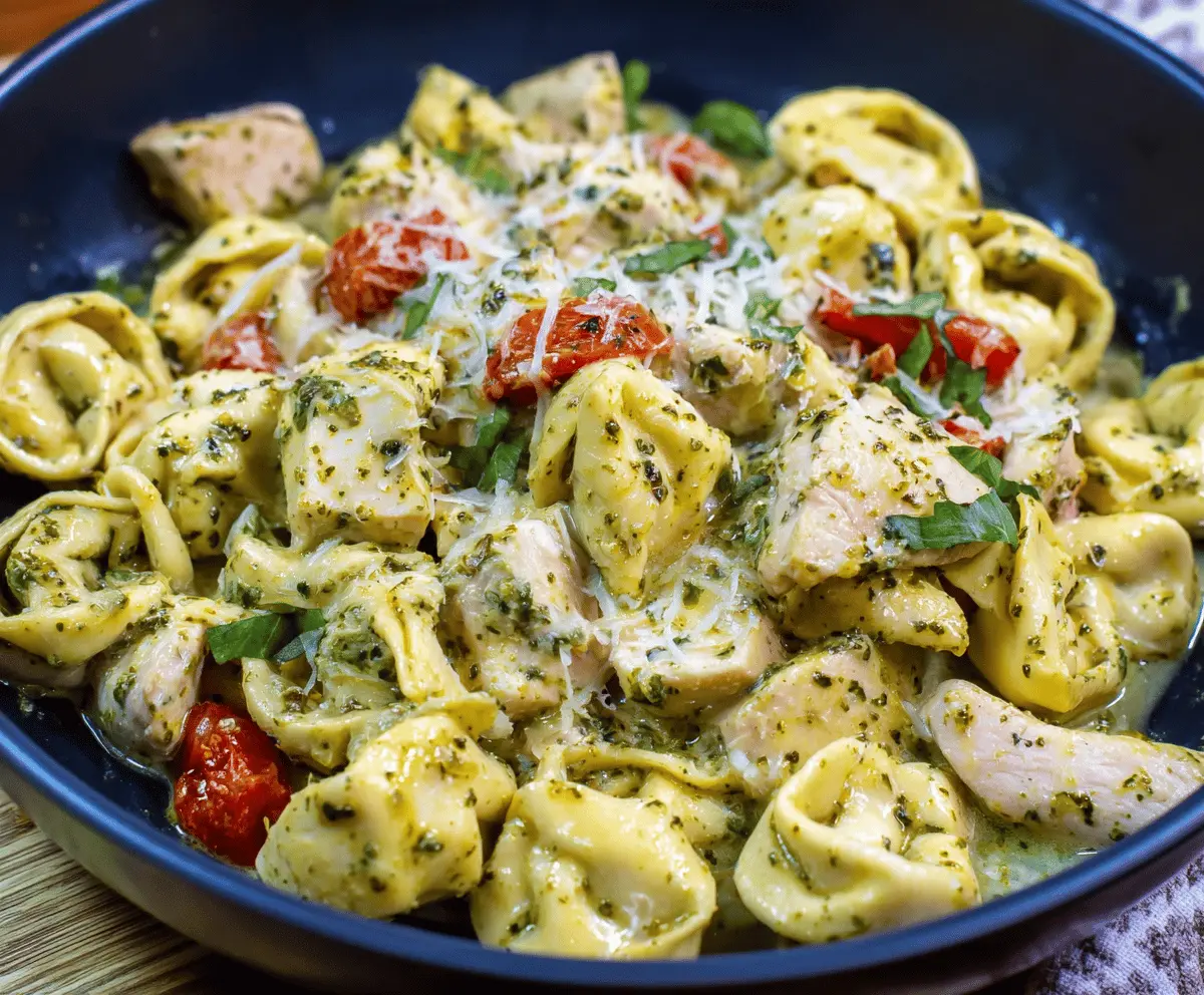 Delicious pesto chicken tortellini dish with fresh basil, melted cheese, and creamy pesto sauce served on a white plate