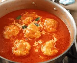Creamy tomato soup garnished with cheese dumplings, served in a bowl with fresh herbs for a comforting and flavorful meal.