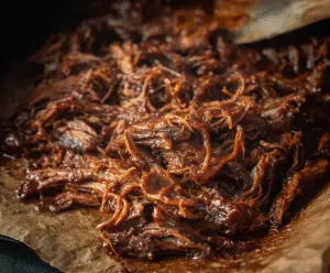 Tender caramelized pulled beef brisket with savory glaze and crispy edges served on a platter.