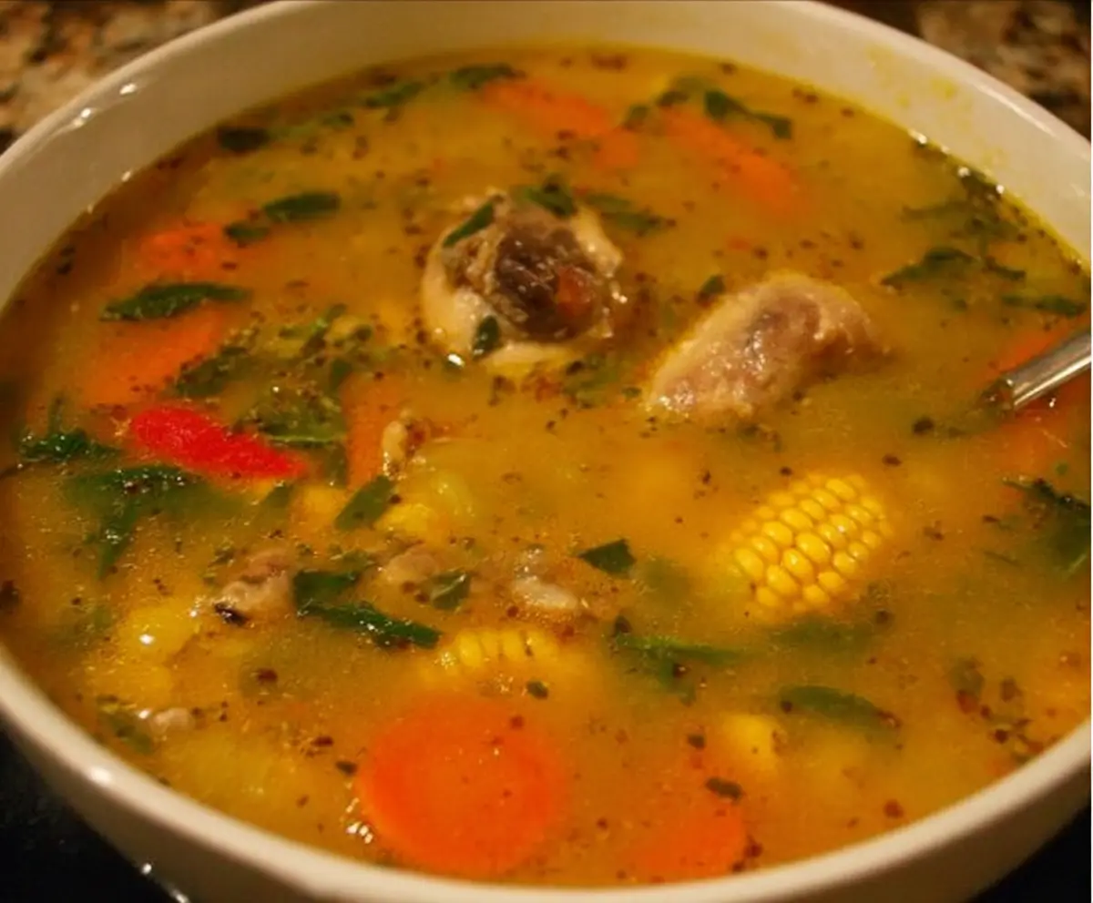 Delicious Jamaican Chicken Soup with fresh vegetables and herbs in a rustic bowl.